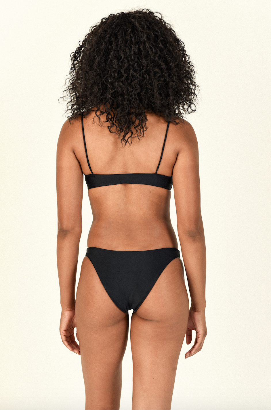 Model standing to the back wearing the Muse Scoop Top and Most Wanted Bottom in Black