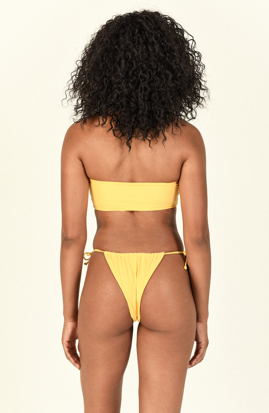 Model standing against white background showing the back of the Ava Bandeau and Lana Bottom in Sand